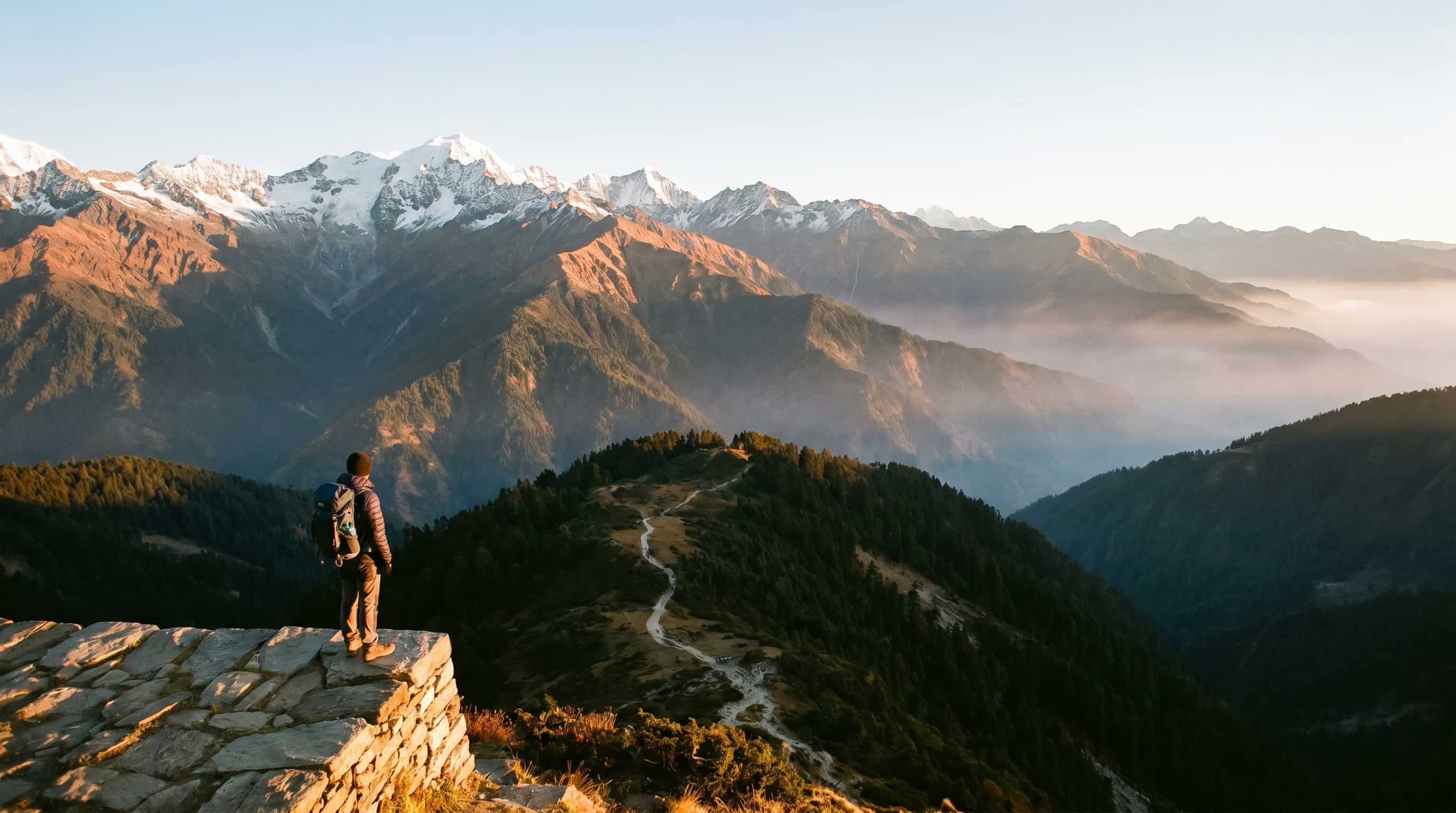 Hiker standing on a mountain ledge overlooking a vast valley landscape on one of the best hiking trails in Asia